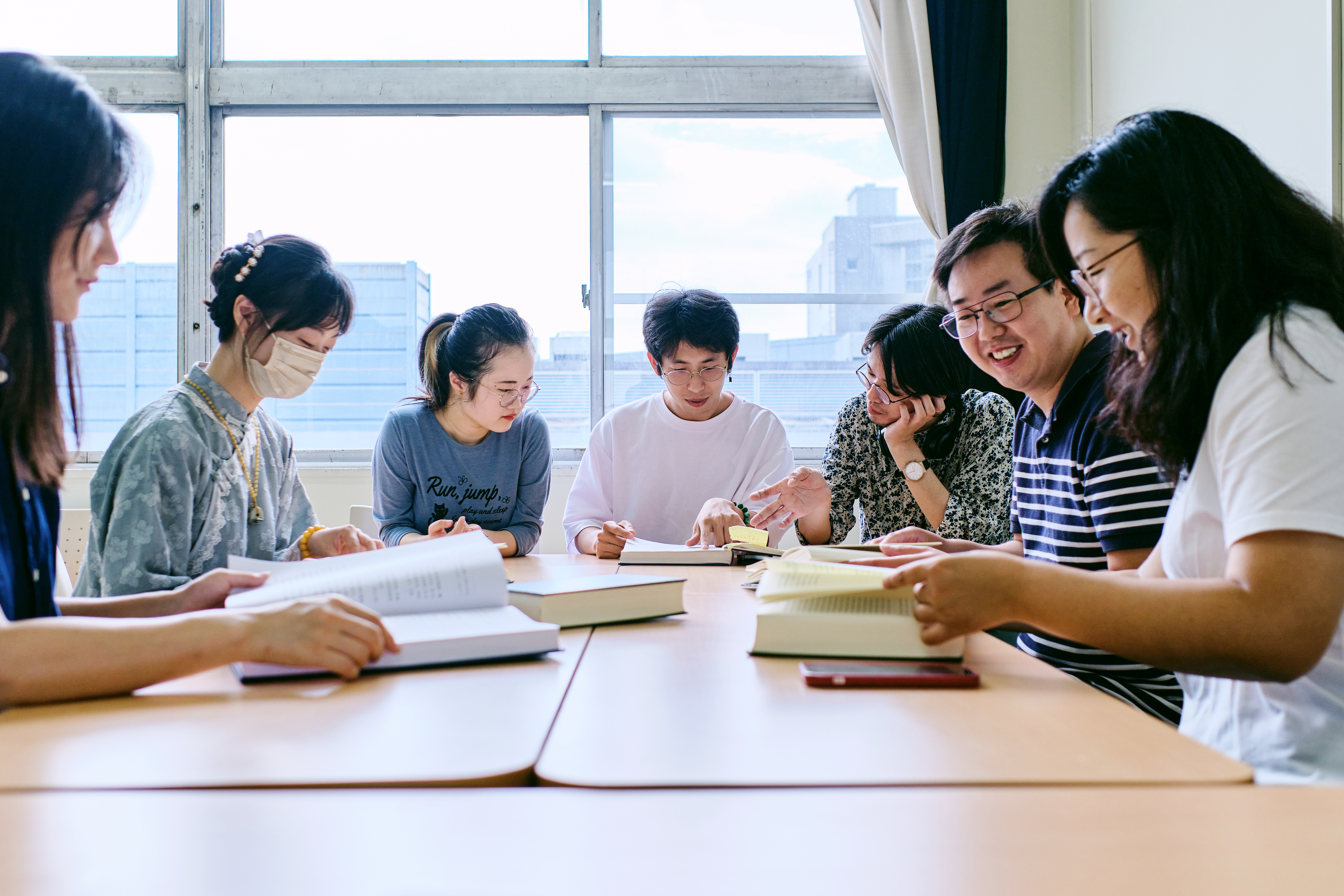 テーブルの上で本を広げながら話し合う学生たち